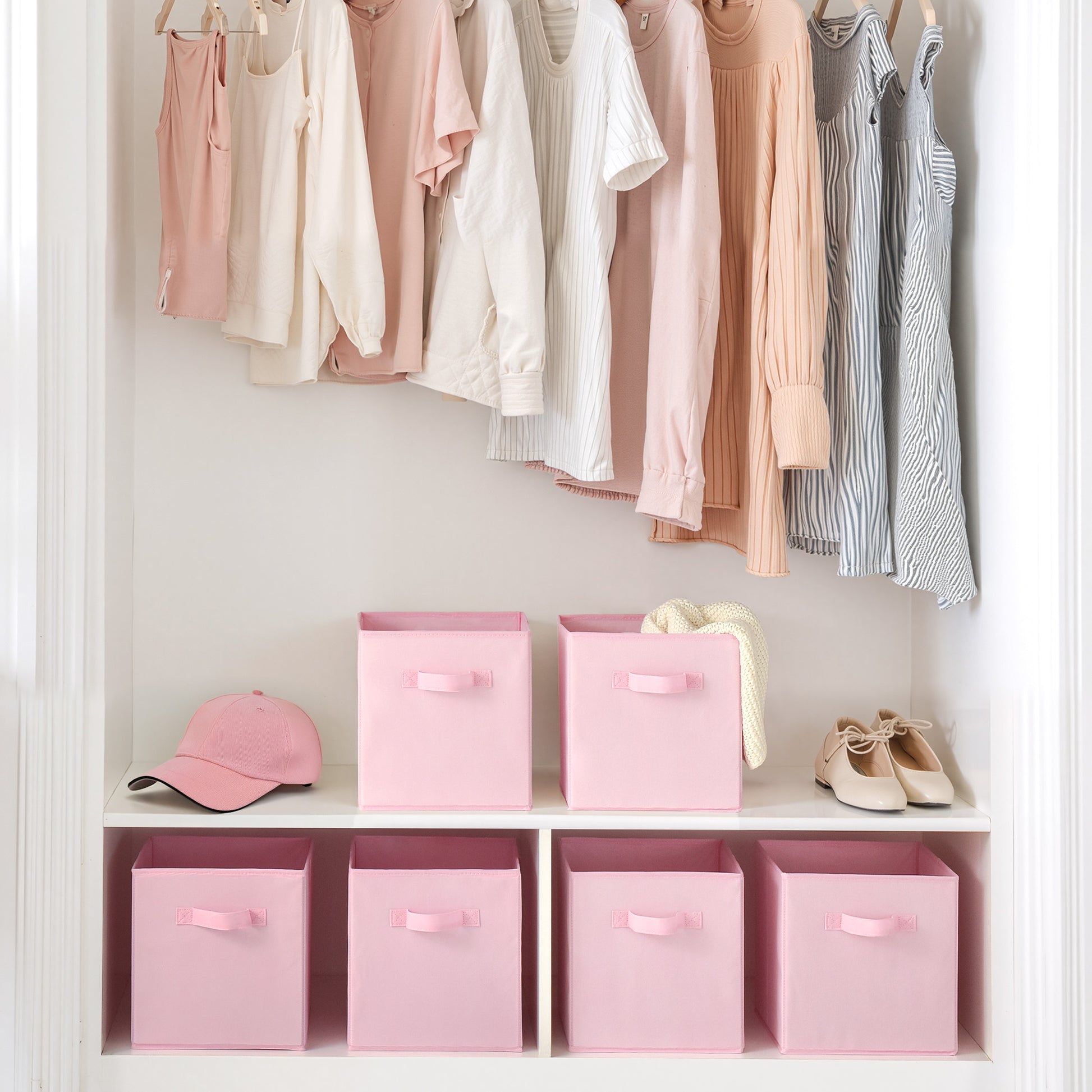 Closet with clothes hanging on a rack and pink storage boxes on shelves.